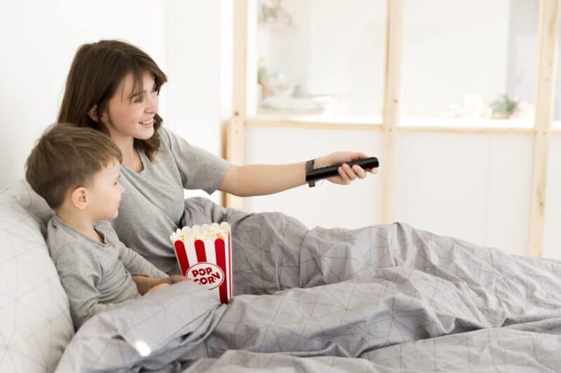 Mama i syn oglądają film razem w łóżku z popcornem.