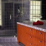 Fioletowa łazienka z prysznicem i drewnianą szafką.