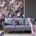 Nowoczesny salon z szarą sofą i kwiatowym muralem na ścianie.