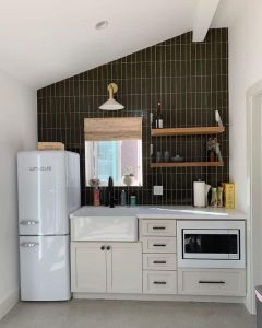 Kuchnia z białymi szafkami, czarną ścianą i drewnianymi półkami.