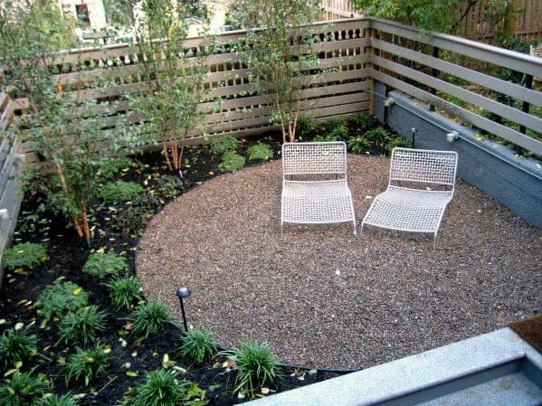 Małe żwirowe patio z dwoma białymi leżakami i roślinami wokół.