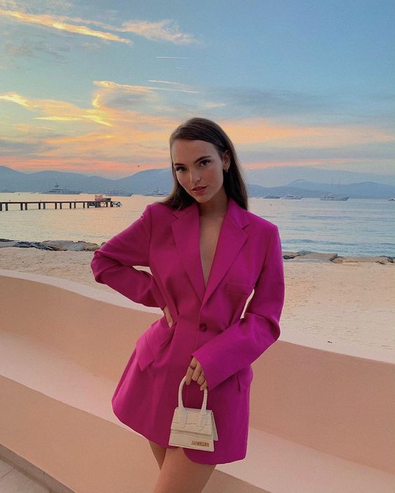 Kobieta w różowej marynarce na plaży podczas zachodu słońca.