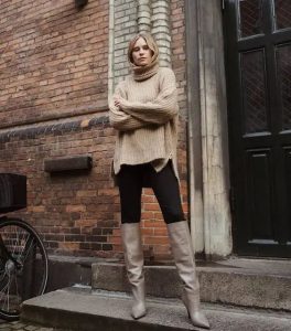 Kobieta w oversize'owym swetrze i wysokich butach na ulicy.