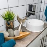 Mała, nowoczesna umywalka na blacie z dekoracjami i rośliną.