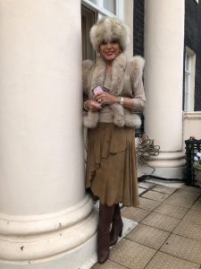 Kobieta w puszystej czapce i eleganckim stroju na zewnątrz.