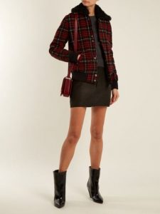 Kobieta w modnej kurtce bomber w kratkę, czarna spódnica i wysokie buty.