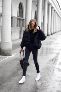 Stylowa kobieta w zimowej kurtce i sneakersach na ulicy.