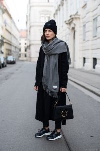 Zadbana mama w zimowym outficie na ulicy, czapka, szalik, buty sportowe.