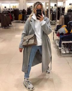 Kobieta w modnym zimowym płaszczu i sneakersach w sklepie odzieżowym.